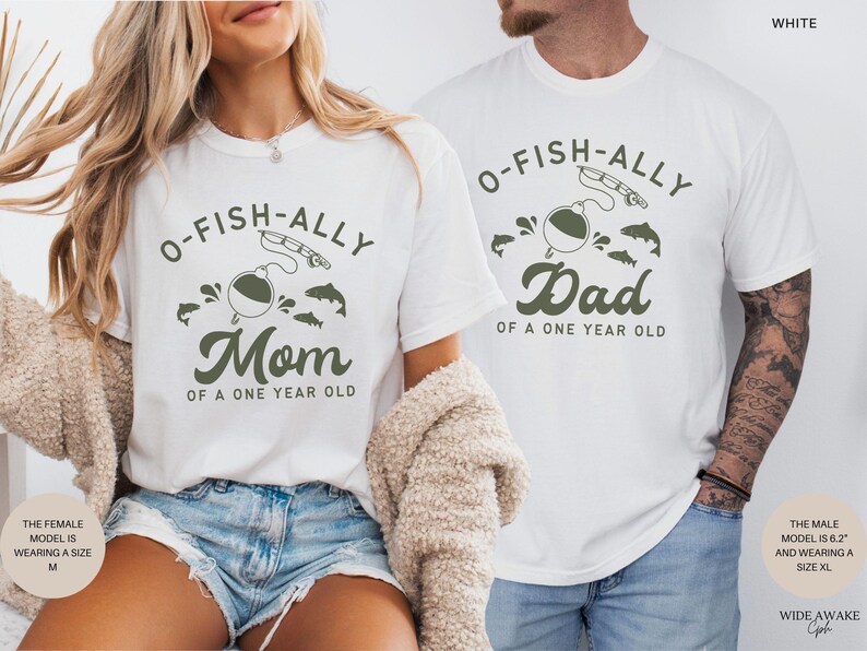 Pu&ograve; includere: T-shirt bianche con grafica a tema pesca. Una maglietta dice "O-FISH-ALLY Mom of a One Year Old" e l'altra dice "O-FISH-ALLY Dad of a One Year Old". Il design include un galleggiante, una canna da pesca e dei pesci.