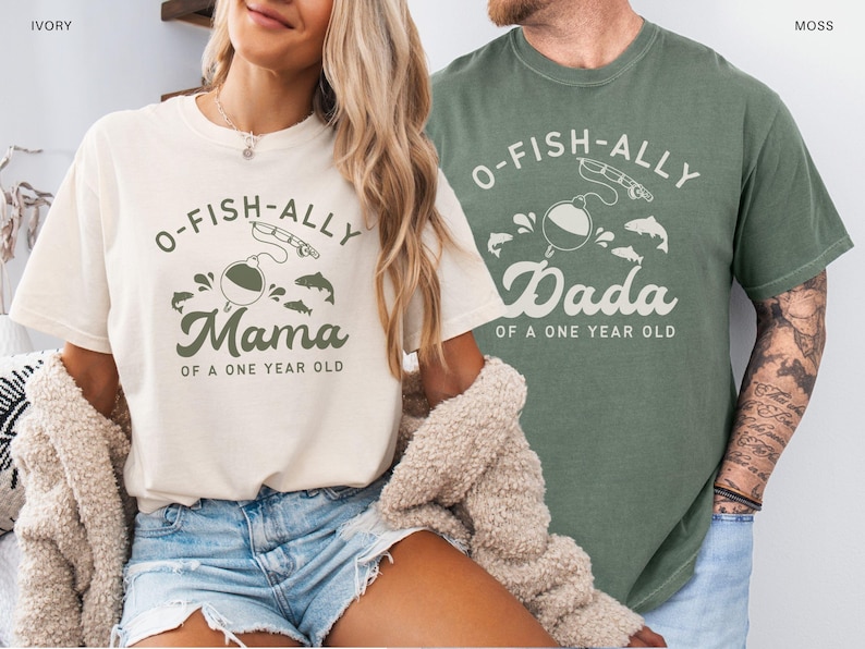 Pu&ograve; includere: Due magliette, una color avorio e una verde muschio, con grafiche a tema pesca abbinate. La maglietta avorio dice "O-Fish-ally Mama of a One Year Old". La maglietta verde muschio dice "O-Fish-ally Dada of a One Year Old".