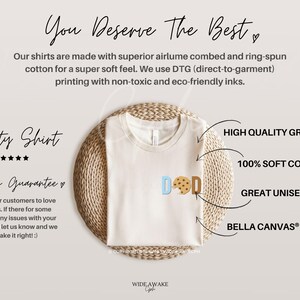 May include: A beige t-shirt with a graphic of a cookie and the word "DOD" in blue, light blue, and brown. The shirt is displayed on a woven mat with text describing the shirt's quality and features, including "High Quality Graphics", "100% Soft Cotton", "Great Unisex Fit", and "Bella Canvas&reg; T-Shirt".