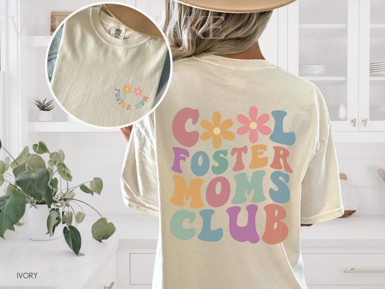 May include: A white t-shirt with the text "Cool Foster Moms Club" in colorful, retro-style letters with flowers. The back of the shirt has a smaller version of the text in a circle with flowers.