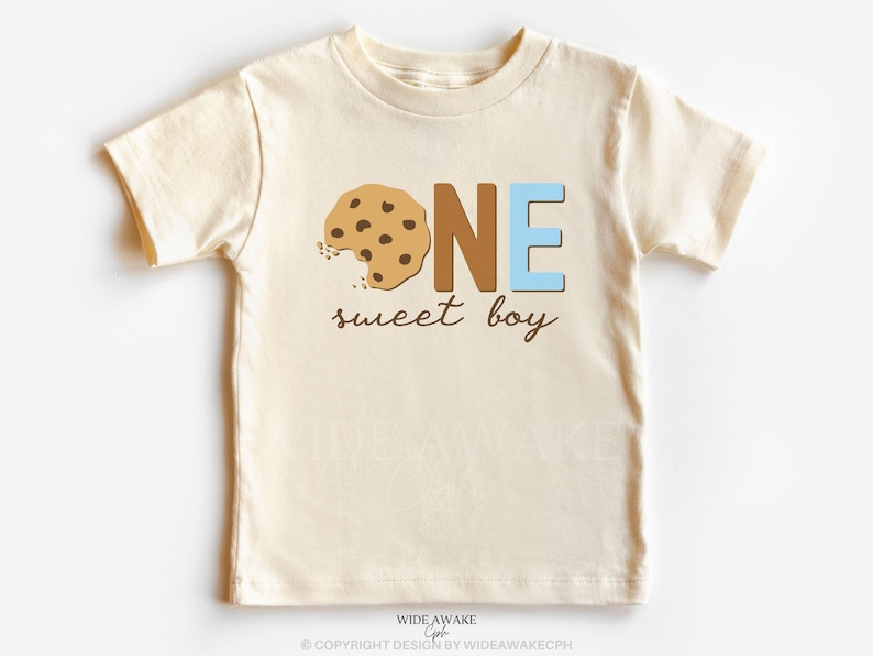 May include: A cream colored short-sleeved t-shirt with the words "ONE sweet boy" and a brown and white cookie graphic.