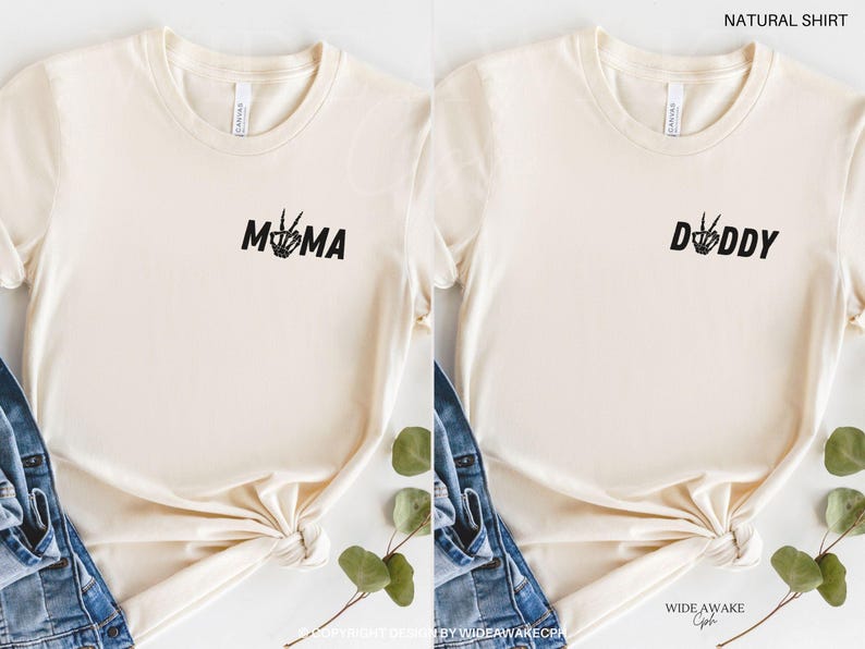 Puede incluir: Dos camisetas de color natural con texto negro. La camiseta de la izquierda dice "MAMA" con un gesto de paz con la mano. La camiseta de la derecha dice "DADDY" con un gesto de paz con la mano.