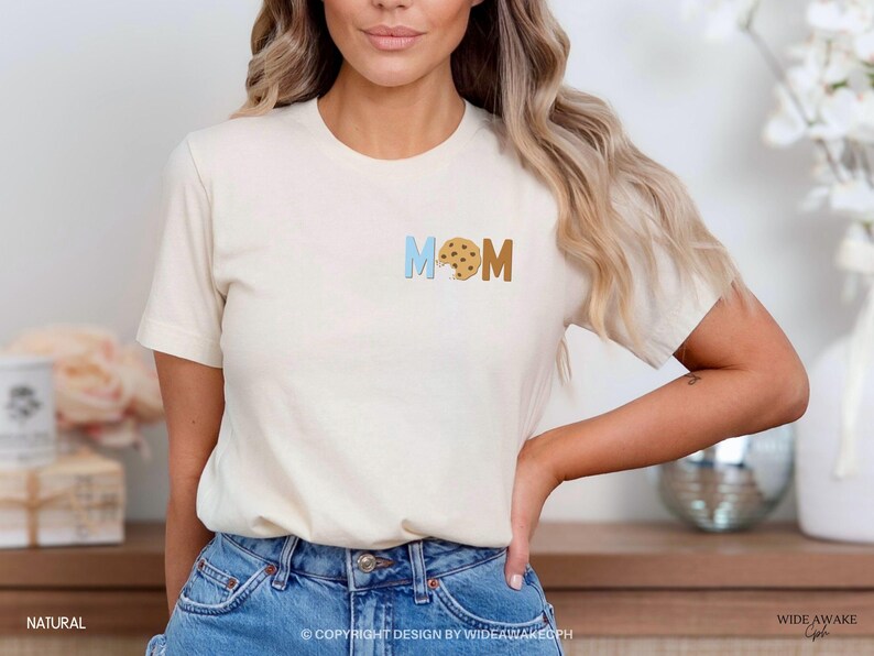 May include: A white t-shirt with the word "MOM" spelled out in blue and brown letters. The "O" is replaced with a chocolate chip cookie.