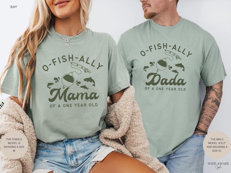 Pu&ograve; includere: Due magliette verde chiaro con la scritta "O-FISH-ALLY Mama" e "O-FISH-ALLY Dada" in verde scuro. Le magliette presentano grafiche a tema pesca, tra cui una canna da pesca, un galleggiante e dei pesci. &Egrave; incluso anche il testo "OF A ONE YEAR OLD".