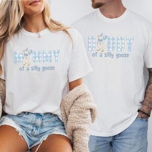 K&ouml;nnte beinhalten: Zwei wei&szlig;e T-Shirts mit einem hellblau-wei&szlig;en Vichy-Karomuster auf den Buchstaben. Das linke T-Shirt zeigt den Text MOMMY of a silly goose mit einer G&auml;nseillustration. Das rechte T-Shirt zeigt den Text DADDY of a silly goose.