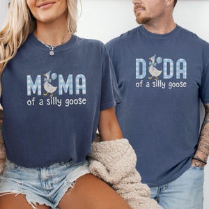 K&ouml;nnte beinhalten: Zwei blau-denimfarbene T-Shirts mit einer wei&szlig;-blau karierten Grafik einer Gans mit Partyhut. Das linke T-Shirt zeigt den Schriftzug MAMA of a silly goose, w&auml;hrend das rechte T-Shirt den Schriftzug DADA of a silly goose in wei&szlig;er Schrift zeigt.