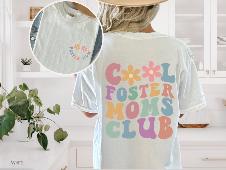 May include: White t-shirt with a colorful graphic that says "Cool Foster Moms Club" with flowers. The shirt also has a smaller graphic on the front that says "Foster Mom" with flowers.