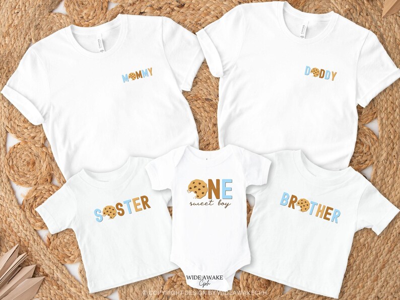 May include: A set of five white t-shirts with blue and brown cookie-themed designs. The shirts say "Mommy", "Daddy", "Sister", "Brother", and "One Sweet Boy".