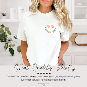 May include: White t-shirt with a colorful graphic that says "Foster Mom" with flowers around the text.