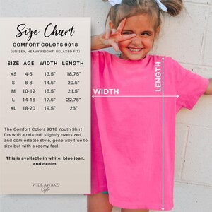K&ouml;nnte beinhalten: Ein leuchtend pinkfarbenes T-Shirt mit kurzen &Auml;rmeln und einer Gr&ouml;&szlig;entabelle. Die Tabelle listet die Comfort Colors 9018 Jugendgr&ouml;&szlig;en von XS bis XL auf, inklusive Alter, Breite und L&auml;nge in Zoll. Der Text beschreibt eine lockere, &uuml;bergro&szlig;e Passform.