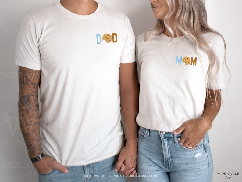 May include: Two white t-shirts with the words "DAD" and "MOM" in blue and brown letters. A cookie graphic replaces the "O" in each word.