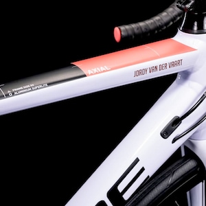 Peut inclure: Gros plan sur un cadre de vélo blanc avec des accents noirs et rouges. Le cadre est marqué "AXIAL" et "JORDY VAN DER VAART".