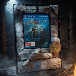 May include: A God of War PS4 video game case displayed within a decorative stone-textured frame. The frame features carved axe motifs, rope accents, and a metal plaque at the bottom labeled Midgard Collector's Edition with MA 15+ rating.