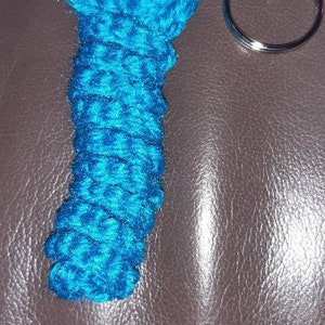 Può includere: Un portachiavi in ​​crochet blu turchese a forma di verme con occhi neri. Il portachiavi è attaccato a un anello portachiavi argentato.
