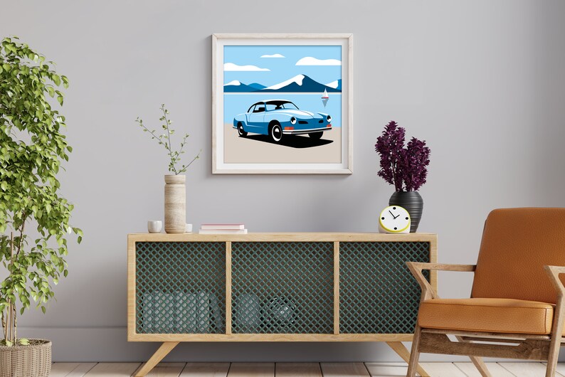 May include: A framed illustration of a blue vintage car driving on a beach with mountains in the background. The car is a Volkswagen Karmann Ghia. The illustration is in a minimalist style with flat colors and simple lines.