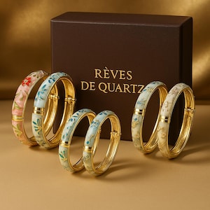 Peut inclure: Plusieurs bracelets dorés ornés de motifs floraux roses, bleus et blancs. Les bracelets sont présentés devant une boîte marron avec le texte "RÊVES DE QUARTZ".