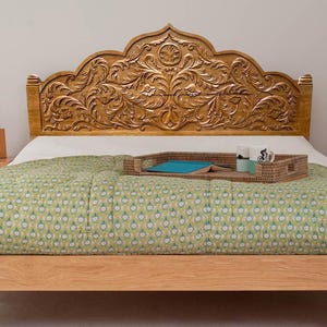 Può includere: Letto in legno con testiera intagliata marrone dorato con un design floreale. Il letto è fatto con una trapunta verde fantasia. Un vassoio intrecciato contiene tazze e un libro. Il letto è largo circa 150 cm.