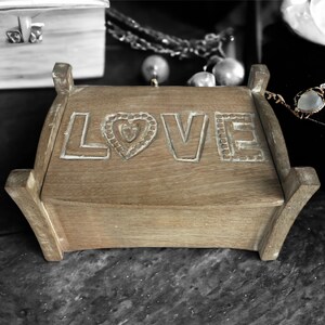 Pu&ograve; includere: Una scatola di legno con la parola "LOVE" intagliata sul coperchio. La scatola &egrave; in legno marrone chiaro e ha un design a forma di cuore al centro della parola "LOVE".