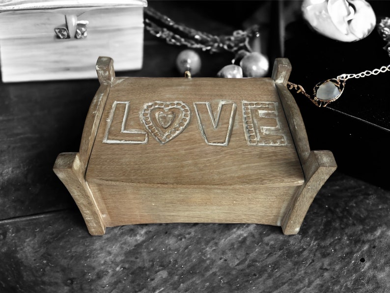 Pu&ograve; includere: Una scatola di legno con la parola "LOVE" intagliata sul coperchio. La scatola &egrave; in legno marrone chiaro e ha un design a forma di cuore al centro della parola "LOVE".