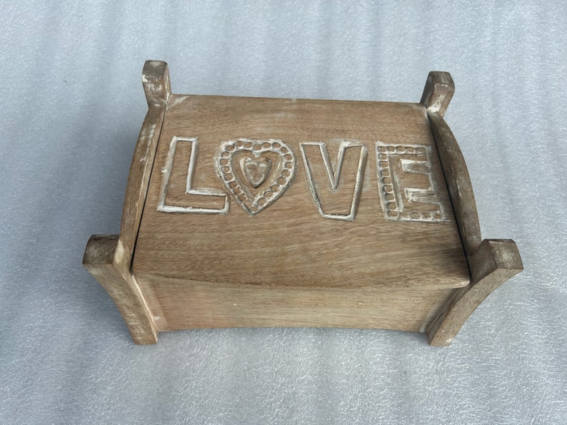 Pu&ograve; includere: Una scatola di legno con un cuore intagliato e la parola "LOVE" sul davanti. La scatola &egrave; di colore marrone chiaro e ha una finitura usurata.