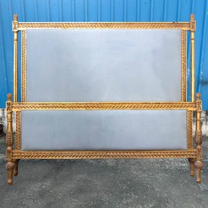 Pode incluir: Uma estrutura de cama dourada com cabeceira e peseira estofadas em cinza. A estrutura apresenta entalhes ornamentados e acabamentos decorativos. A estrutura da cama é um design clássico, adequado para um quarto.