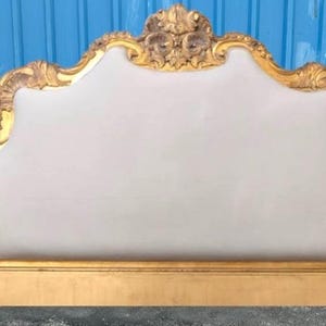May include: A gold-framed headboard with a light gray upholstered center. The ornate gold frame features floral and scroll details. The headboard sits on a matching gold base, creating a luxurious bedroom furniture piece.