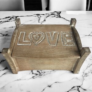 Pu&ograve; includere: Una scatola di legno con la parola "LOVE" intagliata sulla parte superiore. La scatola &egrave; di colore marrone chiaro e ha un cuore intagliato al centro della parola.