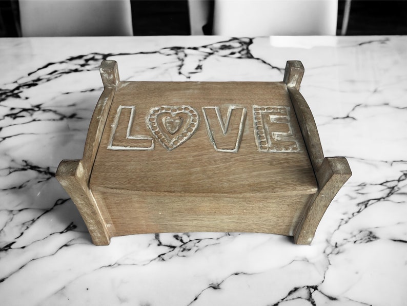 Pu&ograve; includere: Una scatola di legno con la parola "LOVE" intagliata sulla parte superiore. La scatola &egrave; di colore marrone chiaro e ha un cuore intagliato al centro della parola.