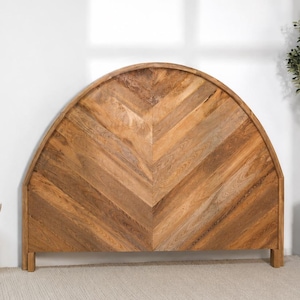 Peut inclure: Une tête de lit semi-circulaire en bois brun clair naturel, présentant un motif à chevrons prononcé qui se rejoint au centre. La pièce possède un bord supérieur arqué lisse et est soutenue par deux pieds en bois courts et rectangulaires.