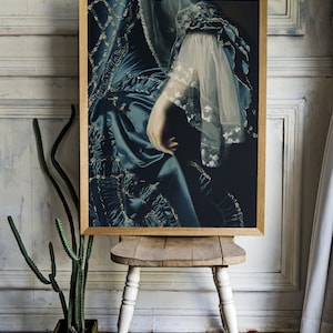 May include: A framed print of a woman's hand and arm wearing a blue and gold dress with lace trim. The dress has a ruffled design and the hand is resting on the fabric.