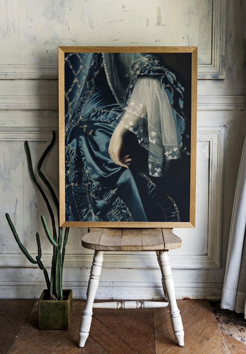 May include: A framed print of a woman's hand and arm wearing a blue and gold dress with lace trim. The dress has a ruffled design and the hand is resting on the fabric.