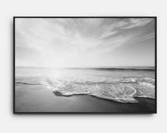 May include: A black and white photograph of a beach scene with waves crashing on the shore. The sky is cloudy and the sun is shining.