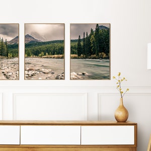 May include: Three framed landscape photographs of a river flowing through a forest with mountains in the background. The photos are hung on a white wall above a wooden dresser.