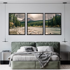 May include: Three framed landscape photographs of a river flowing through a forest with mountains in the background. The photos are hung on a white wall above a green upholstered bed.