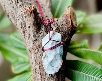 Pode incluir: Um pingente de cristal azul e branco envolto em um cordão vermelho, pendurado em um galho de árvore.