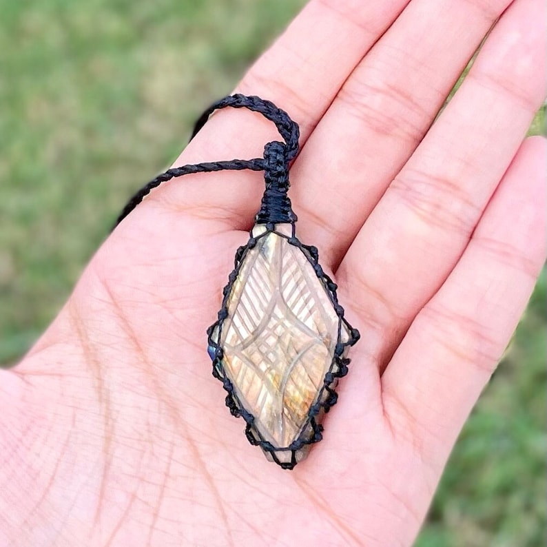 Pode incluir: Um colar de cord&atilde;o preto com um pingente em forma de diamante que apresenta uma pedra de labradorita esculpida com um padr&atilde;o geom&eacute;trico.