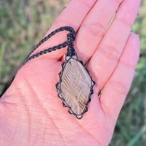 Pode incluir: Um pingente de cristal transparente com um cord&atilde;o de macram&eacute; preto. O cristal tem um padr&atilde;o &uacute;nico de linhas e redemoinhos.