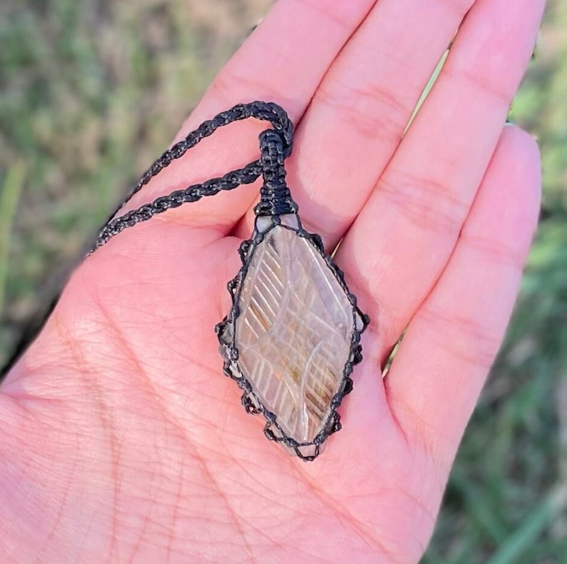 Pode incluir: Um pingente de cristal transparente com um cord&atilde;o de macram&eacute; preto. O cristal tem um padr&atilde;o &uacute;nico de linhas e redemoinhos.