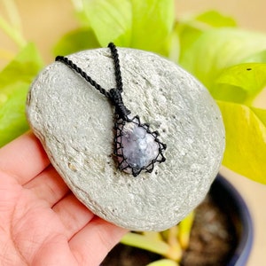 May include: A black cord necklace with a silver and purple gemstone pendant. The pendant is wrapped in black cord and has a starburst design.