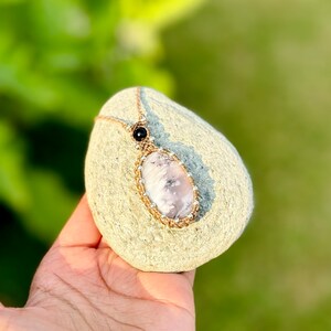 以下が含まれることがあります： 黒色のビーズのアクセントが付いたピンクと白のアゲートの宝石のペンダントで、銀色のビーズが付いたマクラメコードで包まれています