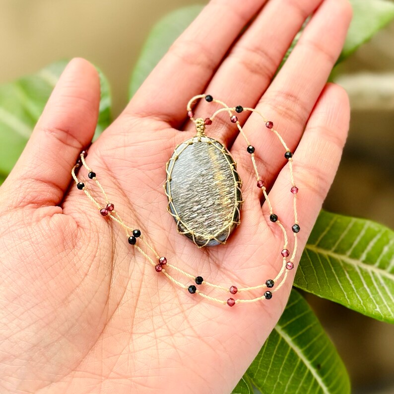 May include: A gold wire wrapped pendant featuring a grey and gold stone, hanging from a double strand necklace with black and burgundy beads.
