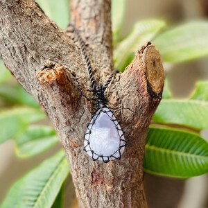 Può includere: Un ciondolo a forma di lacrima in agata color lilla chiaro con un cordoncino in macramé nero.