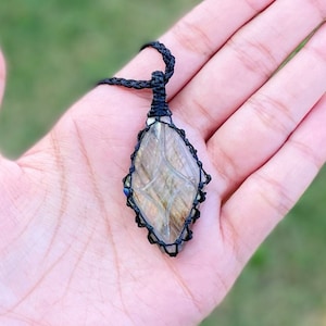 Pode incluir: Um colar de cord&atilde;o preto com um pingente de pedra de labradorita. O pingente &eacute; envolto em cord&atilde;o de macram&eacute; preto e tem a forma de um diamante.