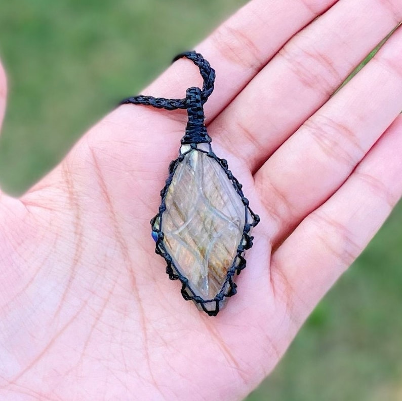 Pode incluir: Um colar de cord&atilde;o preto com um pingente de pedra de labradorita. O pingente &eacute; envolto em cord&atilde;o de macram&eacute; preto e tem a forma de um diamante.