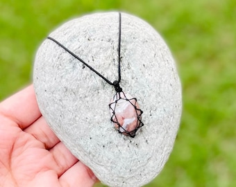 Könnte beinhalten: Eine Halskette mit einem Anhänger aus rosa und weißem Achat, einem schwarzen Band und einem Makramee-Knotenmuster.