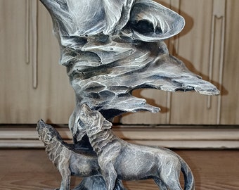 May include: A gray and brown wolf sculpture with a howling expression. The wolf is standing on a rocky base with two smaller wolves at its feet.