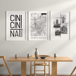 Puede incluir: Tres impresiones enmarcadas en blanco y negro en una pared blanca. La impresión de la izquierda tiene el texto "CINCINATI OHIO" en negro. La impresión del medio es un mapa de Cincinnati, Ohio con las coordenadas "39.1031°N / 84.5120°W". La impresión de la derecha es un collage de fotos en blanco y negro de monumentos de Cincinnati.