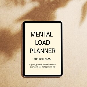 Peut inclure: Une tablette numérique à bordure noire affiche le texte "MENTAL LOAD PLANNER" et "FOR BUSY MUMS". La tablette est posée sur une surface beige avec des ombres de feuilles.