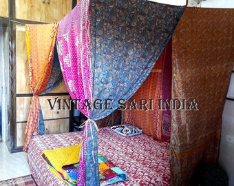 May include: A bed with a canopy made of colorful vintage saris. The canopy is draped over the bed and tied at the corners. The bed has a red and white patterned bedspread and a yellow quilt on top. The bed is in a room with a wooden closet and a green rug on the floor. The text "Vintage Sari India" is visible in the image.