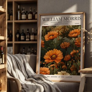 Peut inclure: Une affiche encadrée avec un motif floral de fleurs orange et de feuilles vertes. L'affiche porte l'inscription "WILLIAM MORRIS COTTON PRINTS EXHIBITION" et "THE ARTISTRY OF 19TH CENTURY". L'œuvre est exposée dans une pièce avec une étagère en bois.